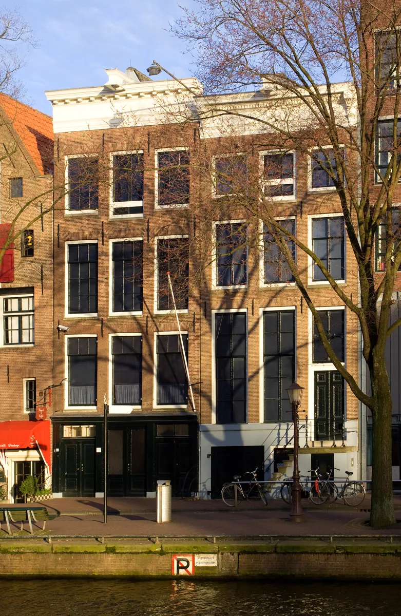 Two plain brick canal houses with tall windows and white cornices on the Prinsengracht, behind a bare tree, with bicycles parked by the water