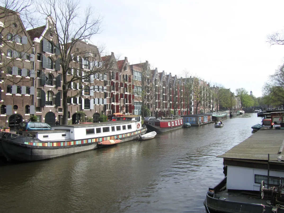 The Brouwersgracht with houseboats moored along it and a row of tall brick warehouses with wooden shutters on the left bank