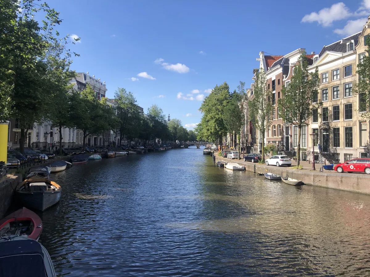 The Keizersgracht on a sunny day, with small boats moored along both banks, tall canal houses on the right and an arched bridge in the distance