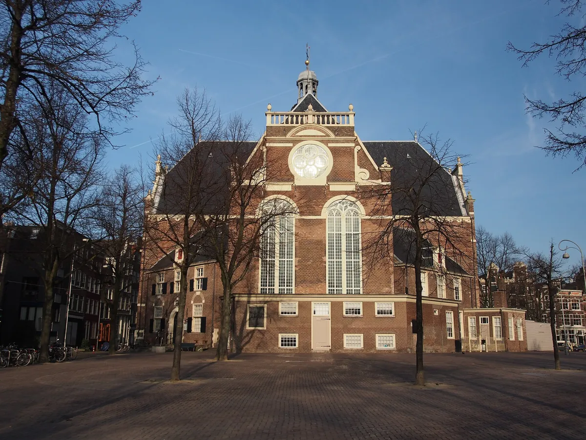 The brick Noorderkerk with a round rose window, two tall arched windows and a small domed tower, seen across an empty paved square with bare trees