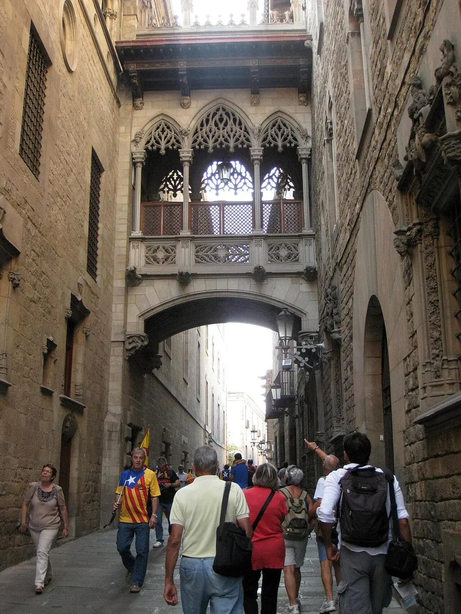 The carved neo-Gothic bridge across Carrer del Bisbe, with walkers in the lane below