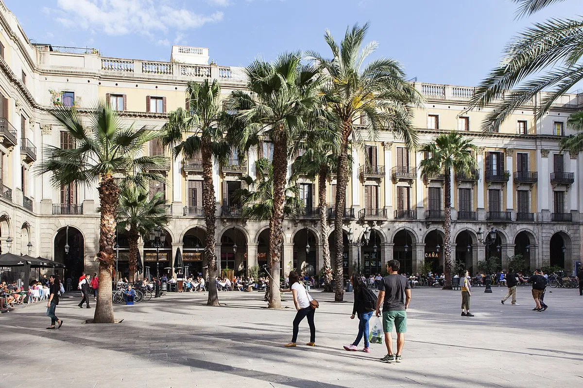 Plaça Reial with palm trees, café tables under the arcades and uniform cream façades