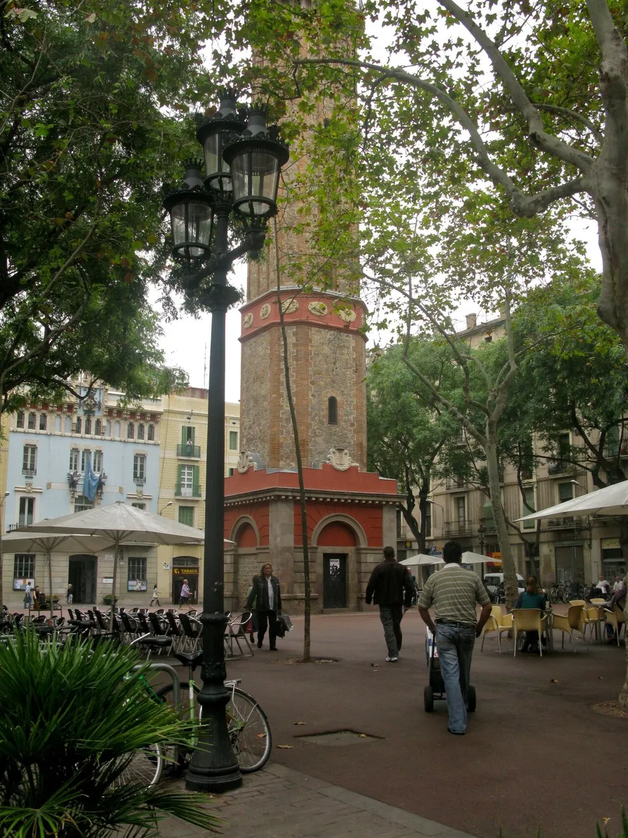 The eight-sided brick and stone bell tower in Plaça de la Vila de Gràcia, seen past a street lamp and café tables