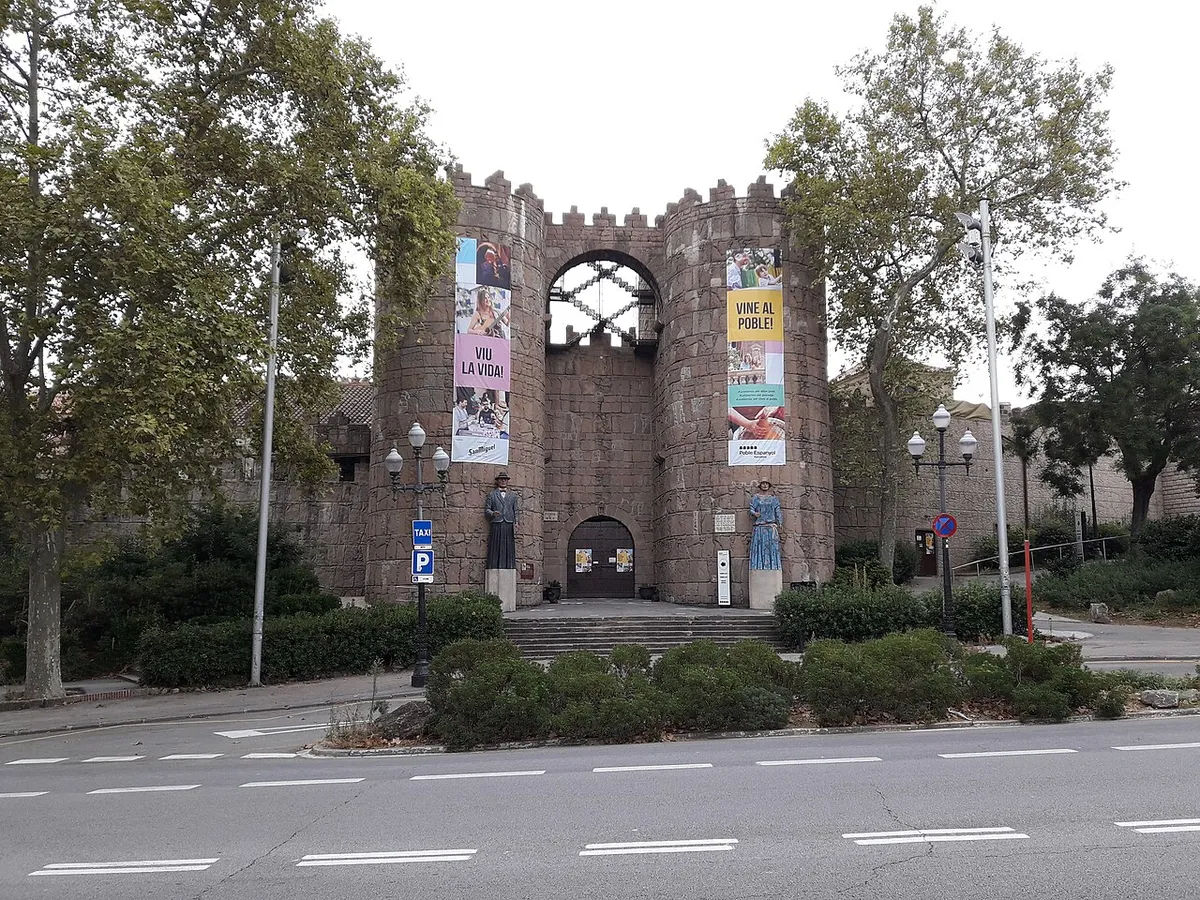 The Porta d'Àvila: a stone gate between two round battlemented towers, seen from the road