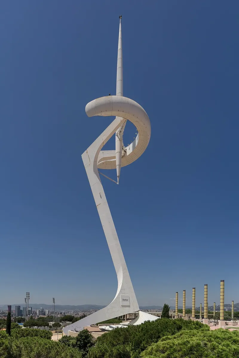 The white leaning steel tower with a curved ring and a tall needle, against a blue sky