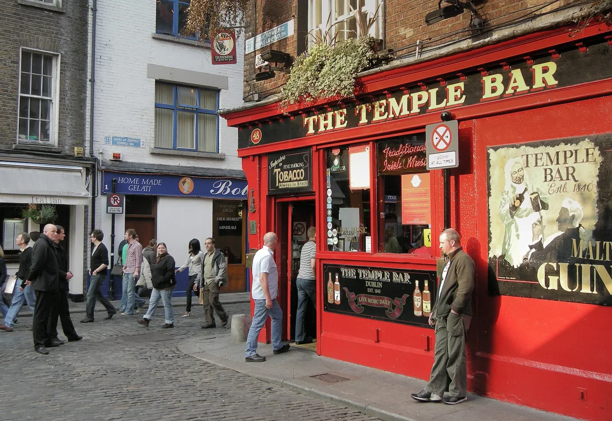 The red front of the Temple Bar pub on a cobbled corner, with gold lettering, a painted Guinness sign and people walking past