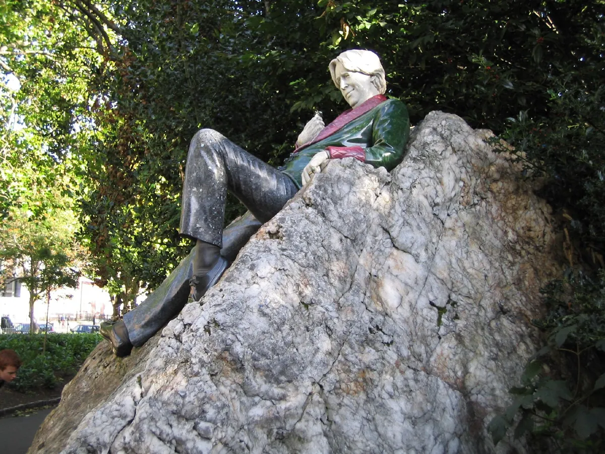 The Oscar Wilde statue in Merrion Square: Wilde in a green jacket with pink collar and cuffs, lounging on a large white quartz boulder under trees