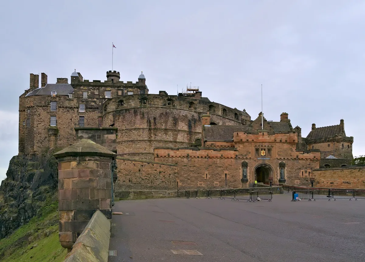 Edinburgh Castle seen across the empty tarmac of the Esplanade: the curved wall of the Half Moon Battery, the Royal Palace on the left and the gatehouse with two statues on the right