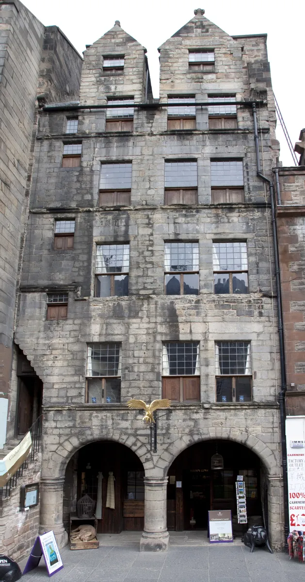 The tall grey stone front of Gladstone's Land, six storeys with twin gables, two round arches at street level and a gilded hawk above them