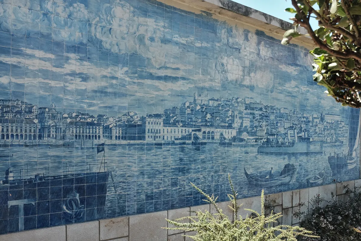 A large blue-and-white tile panel on a wall, showing a city waterfront with arcaded buildings, rooftops climbing a hill, and ships and boats on the river
