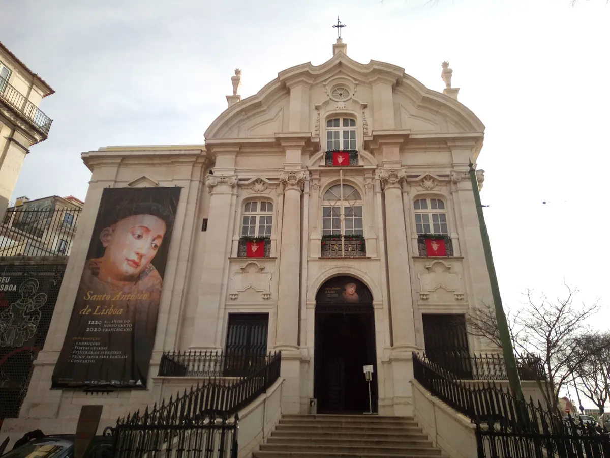 The pale stone front of the church of Santo António, with a curved pediment, three upper windows and a flight of steps up to the door