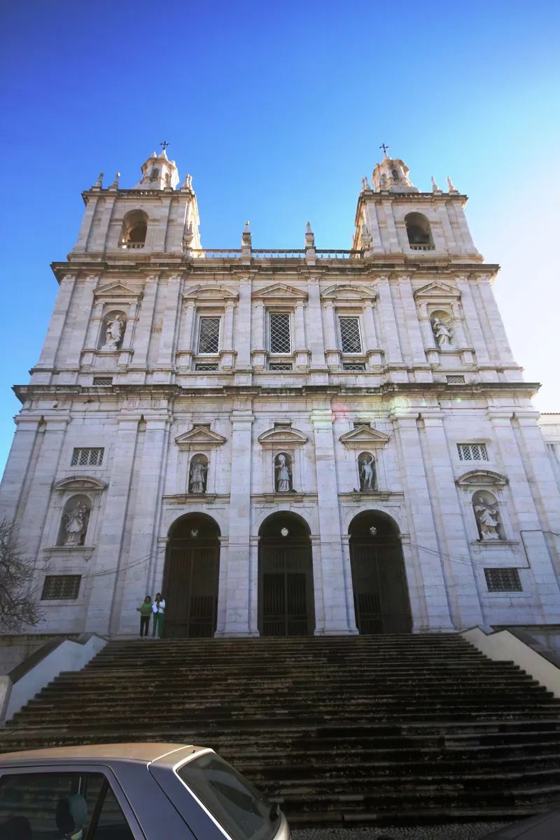 The tall white front of São Vicente de Fora, with two towers, rows of statues in niches and three arched doors at the top of a wide flight of steps