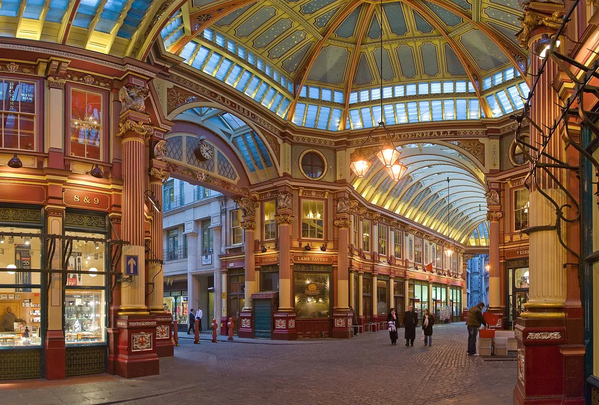 Inside Leadenhall Market: cobbled lanes under a painted glass and iron roof, with red and cream shopfronts, a clock and hanging lamps