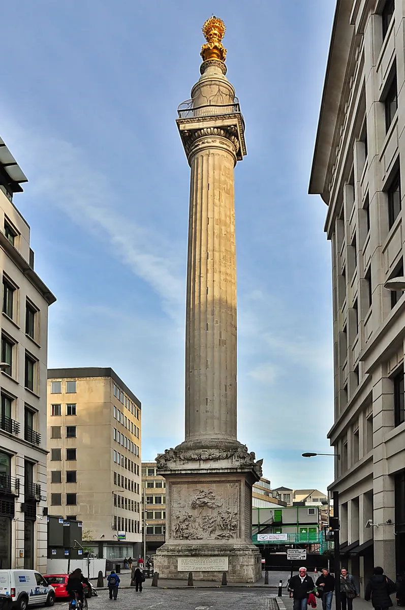 The Monument, a tall fluted stone column with a carved base and a gilded urn of flames on top, standing in a street between office buildings