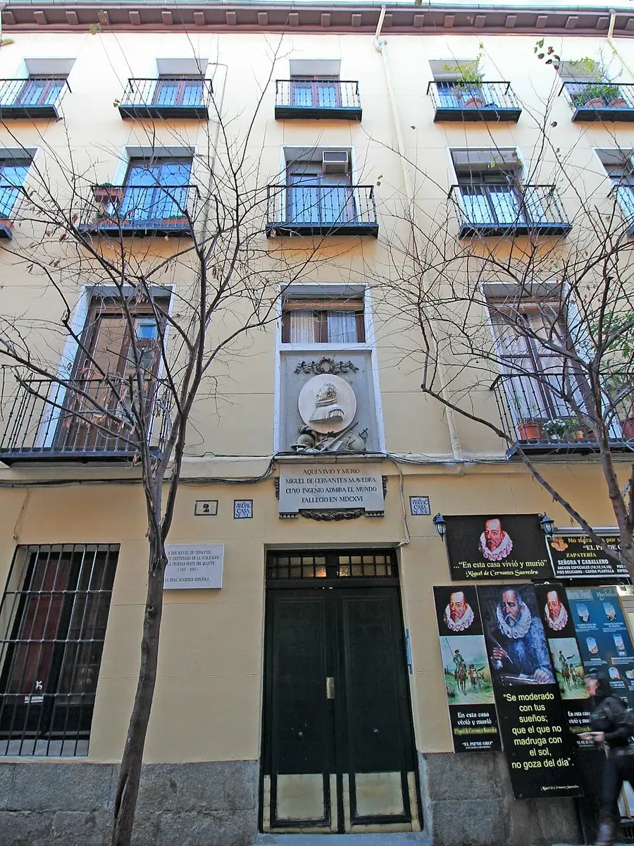 A four-storey yellow apartment building at Calle de Cervantes 2, with a round stone medallion of Cervantes above the main door and plaques beside it