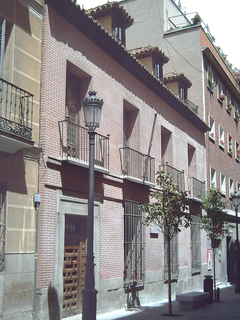 The plain brick-coloured front of Lope de Vega's house on Calle de Cervantes, with a stone base, small iron balconies and a wooden door, beside a street lamp
