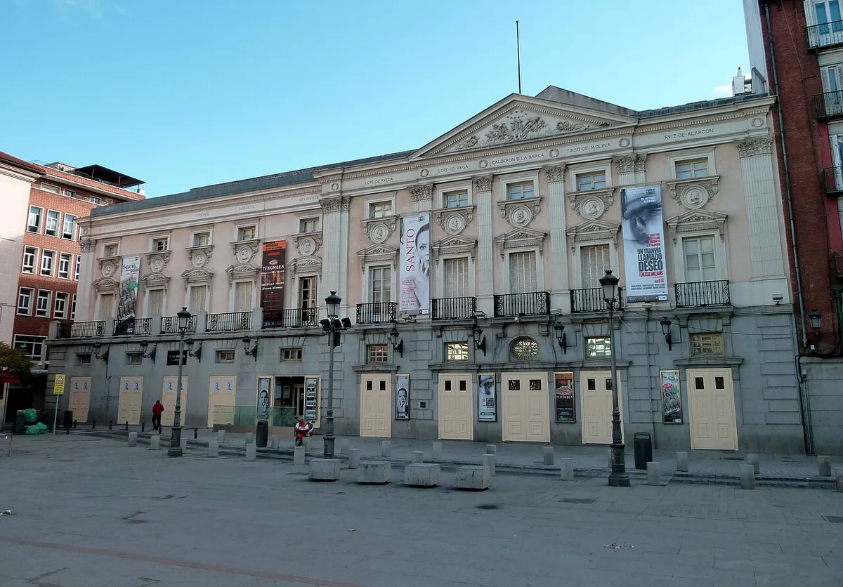 The long pale front of the Teatro Español, with a pediment, balconies and street lamps, seen across the paving of Plaza de Santa Ana
