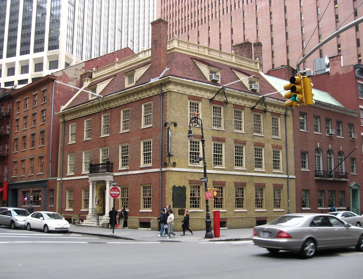 Fraunces Tavern, a three-storey corner building of red and yellow brick with a hipped roof, dormer windows and a white columned porch, among taller buildings