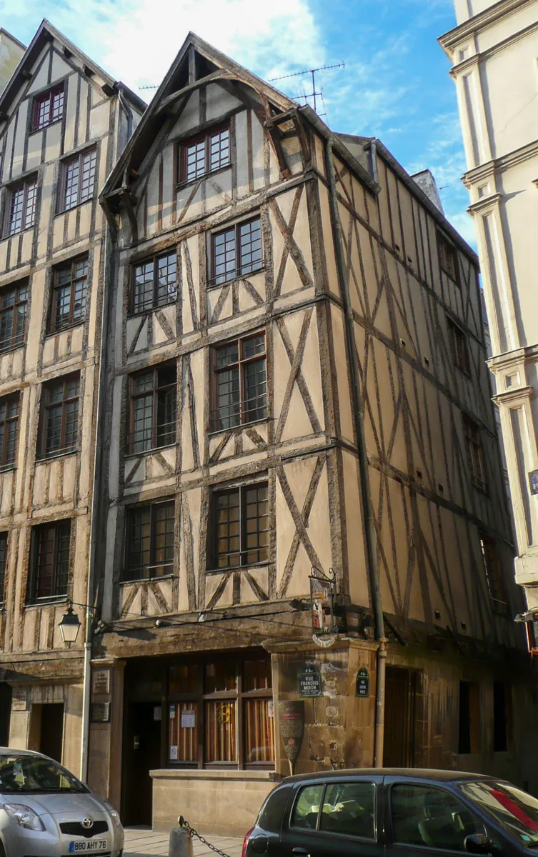 Two tall half-timbered houses with dark diagonal beams, small-paned windows and steep gables, beside a plainer stone building
