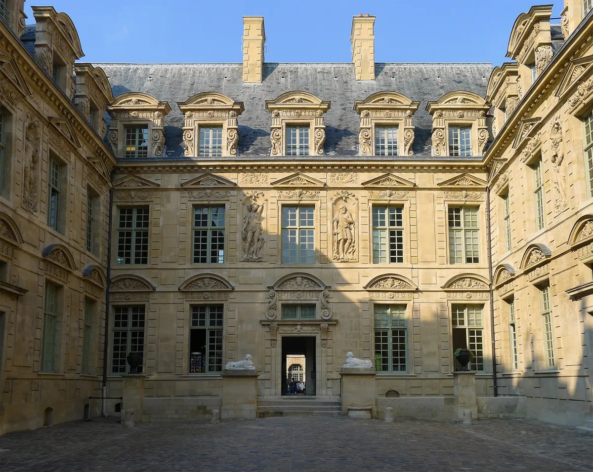 The cobbled courtyard of the Hôtel de Sully, with carved stone fronts, tall statues between the windows, ornate dormers and two stone sphinxes by the central doorway