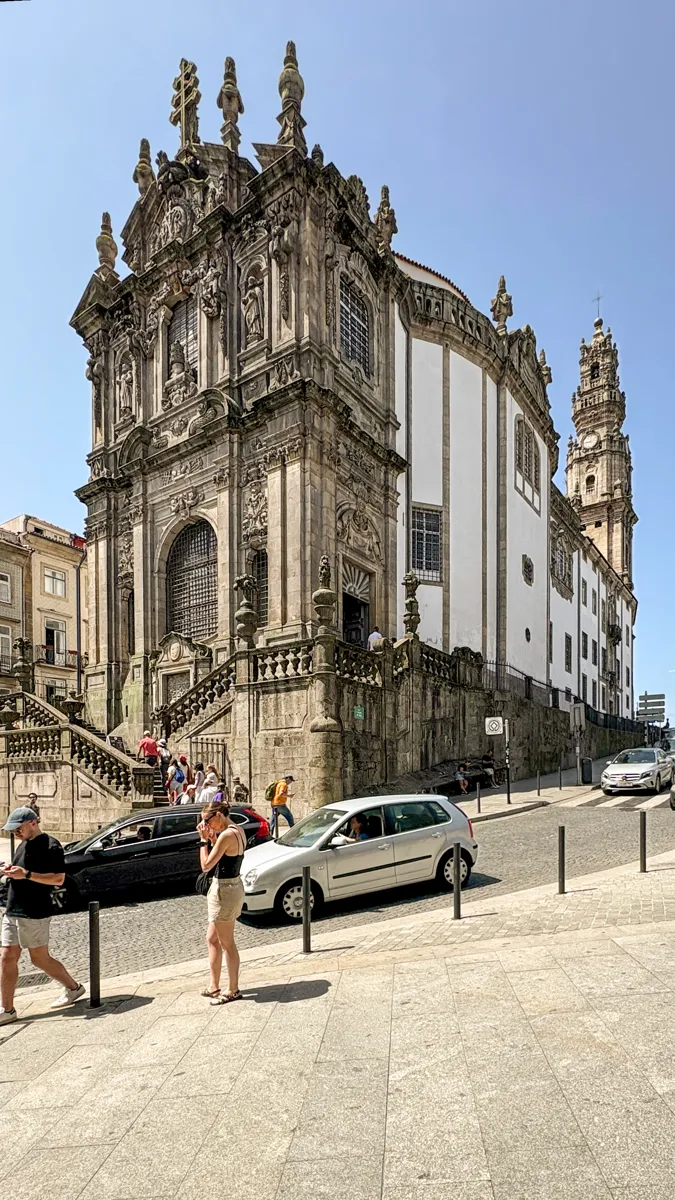 The carved granite front of the Clérigos church at the top of a sloping street, with the tall Baroque bell tower rising behind it
