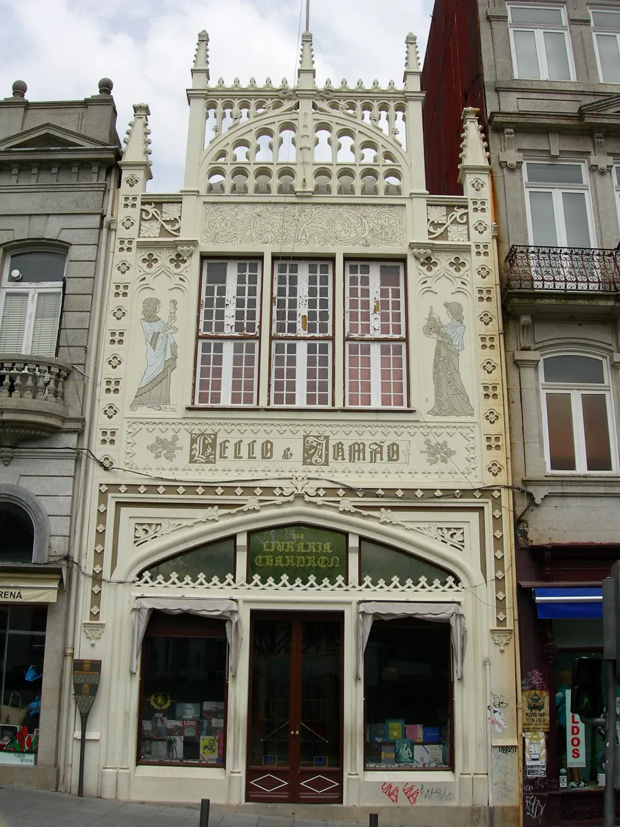 The narrow white neo-Gothic front of Livraria Lello, with pinnacles on top, two painted figures beside the upper windows and a wide arched shop window below
