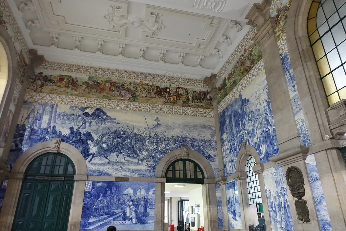 The entrance hall of São Bento station, its walls covered in large blue-and-white tile pictures of historical scenes under a coloured frieze and a white stucco ceiling