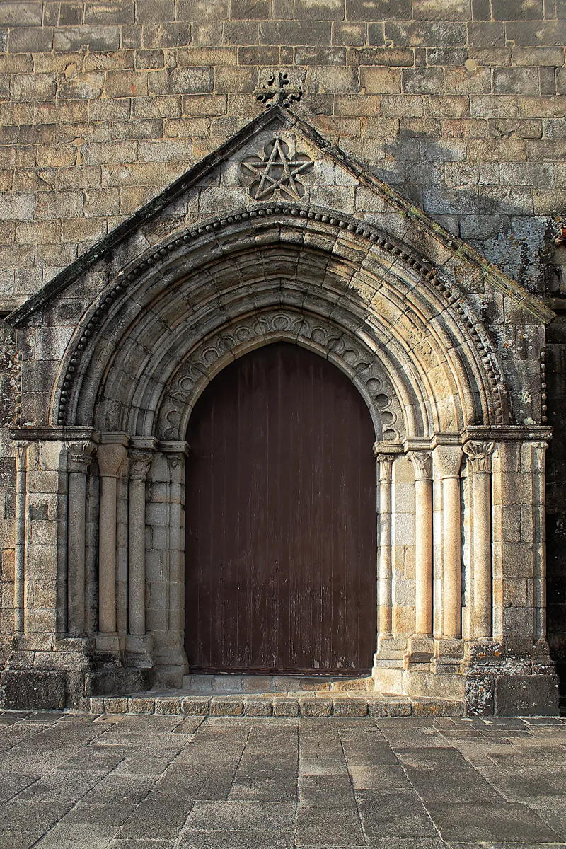A pointed Gothic stone doorway with several carved arches and a wooden door, under a triangular gable with a five-pointed star