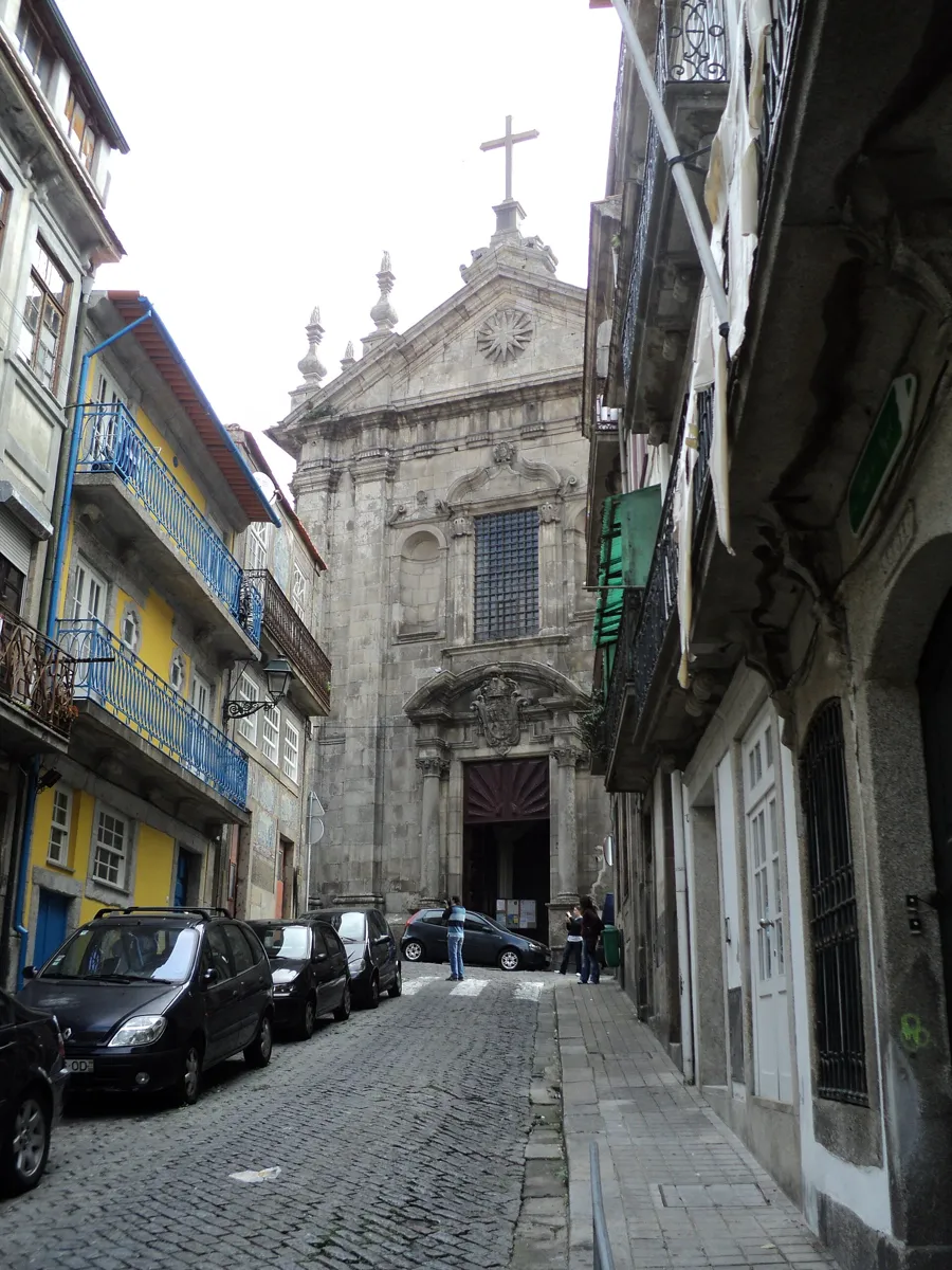A narrow cobbled street between old houses with iron balconies, ending at the grey stone front of a church
